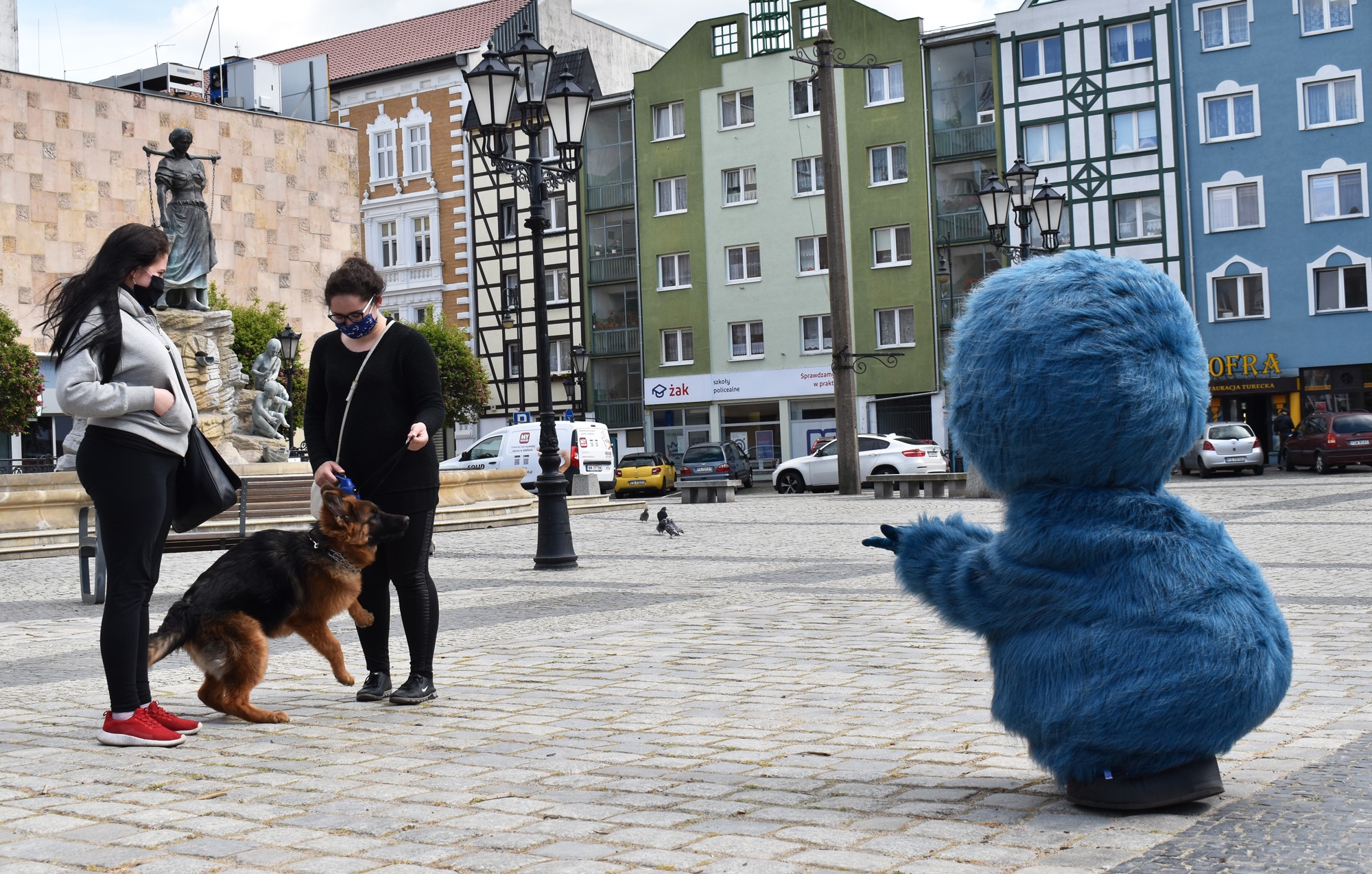 Na fotografii widnieje maskotka stworek Staluś pozujący do zdjęcia w Gorzowie Wielkopolskim. Obok maskotki dwie kobiety i pies